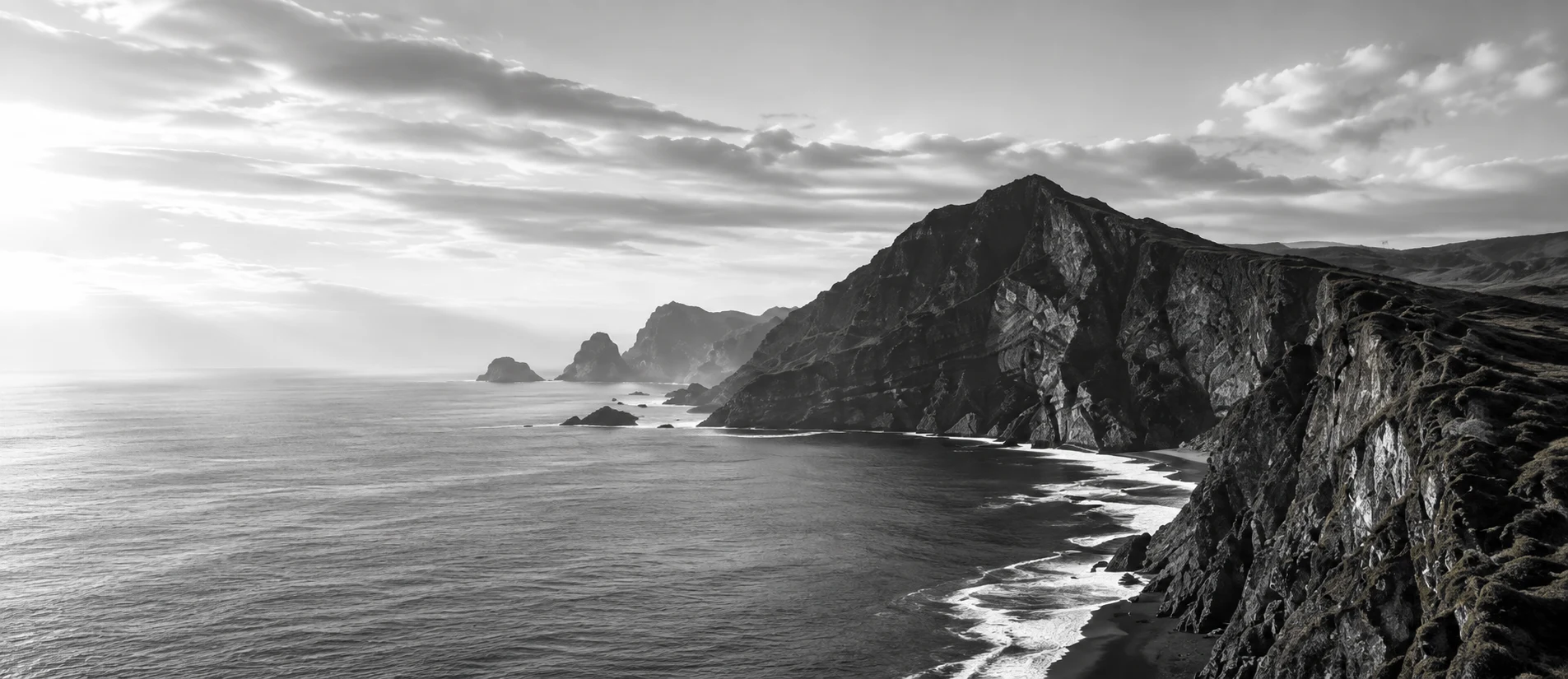 A headland of dark cliffs meeting a bright, calm sea